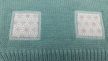 Détail des motifs en tissu sur un pull bébé en laine mérinos extrafine